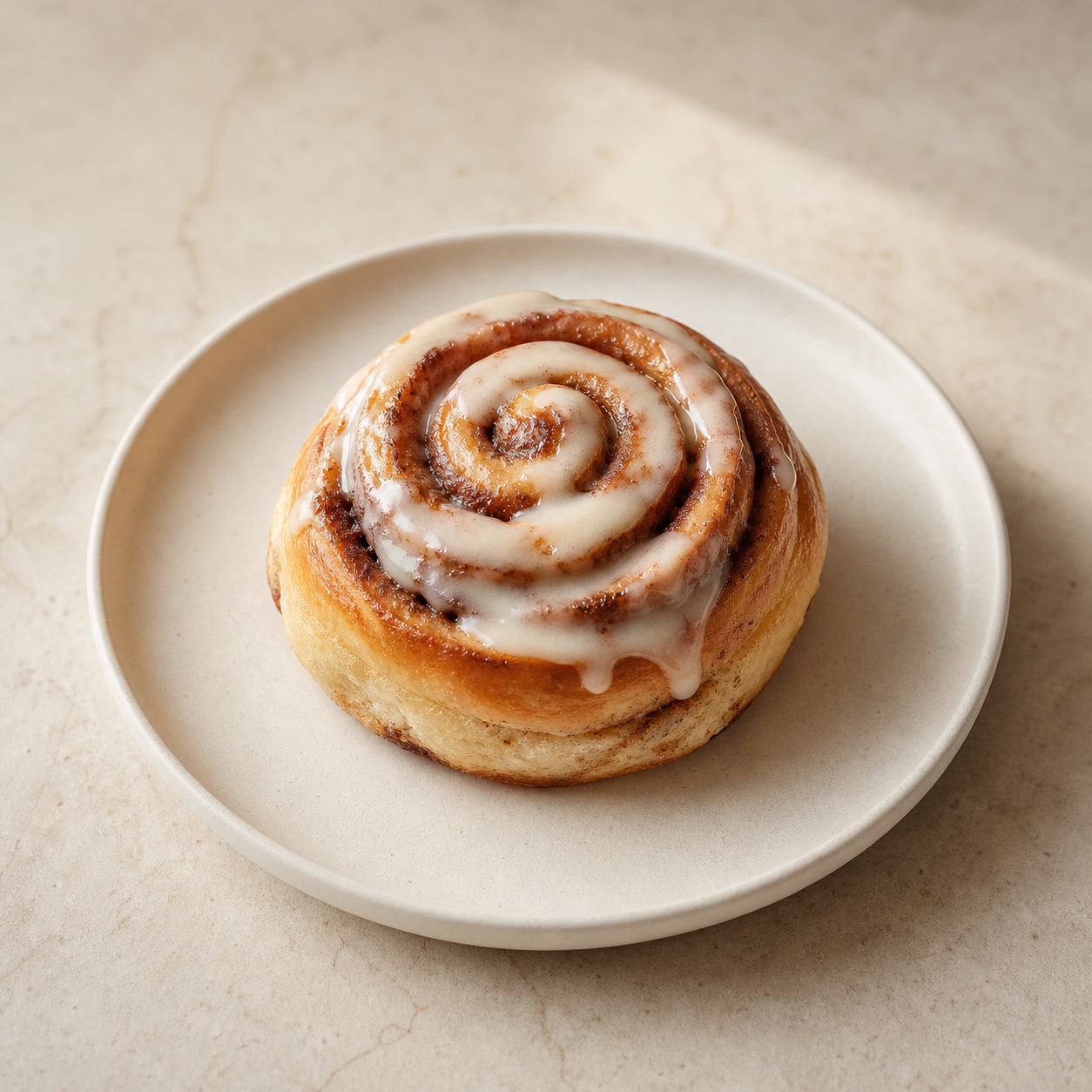 Cinnamon roll with a light glaze on a cream ceramic plate